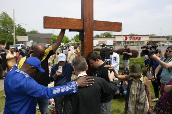 FILE - A group prays at the site of a memorial for the victims of the Buffalo supermarket shooting outside the Tops Friendly Market on Saturday, May 21, 2022, in Buffalo, N.Y. The victims of the mass shooting will be honored with a permanent memorial in the neighborhood. Gov. Kathy Hochul and Mayor Byron Brown on Friday, Oct. 21, 2022,  announced the creation of a commission tasked with planning and overseeing construction of a monument in East Buffalo. (AP Photo/Joshua Bessex, File)