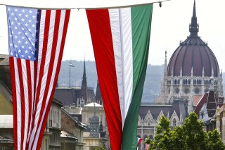 FILE - American and Hungarian national flags fly in downtown Budapest, Hungary, on Wednesday, June 21, 2006, with the historical parliament building at the background. The United States is imposing travel restrictions on citizens of Hungary over concerns that the identities of nearly 1 million foreigners granted Hungarian passports over nine years were not sufficiently verified. That's according to the U.S. Embassy and a government official. (AP Photo/Alexander Zemlianichenko, File)
