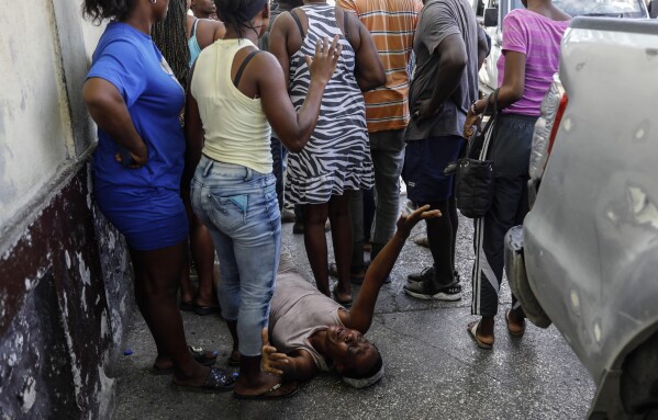A woman lies on the sidewalk as she mourns a family member shot by unknown assailants while sitting on his motorcycle in the Delmas neighborhood of Port-au-Prince, Haiti, Friday, March 8, 2024 (AP Photo/Odelyn Joseph)
