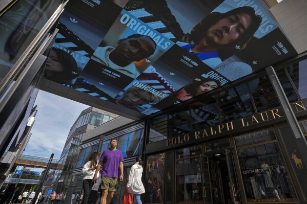 People walk through a screen advertisement of an Adidas sportswear at an outdoor shopping mall in Beijing Wednesday, Sept. 20, 2023. Leading Chinese planners voiced confidence Wednesday in the outlook for the world's second-largest economy, holding key interest rates steady amid signs of improvement in some areas such as services. (AP Photo/Andy Wong)