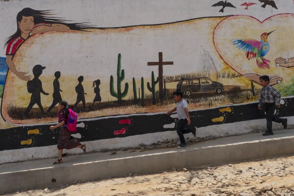 Children run past a mural memorializing 19 locals who were shot and burned in Camargo, Mexico, as they attempted to migrate to the U.S., in Comitancillo, Guatemala, Tuesday, March 19, 2024. In this small town, nearly two dozen local migrants have died in recent mass tragedies: either asphyxiated in the trailer in San Antonio, Texas, in June 2022 or shot and set afire by rogue police officers in Camargo, Mexico, in January 2021. (AP Photo/Moises Castillo)