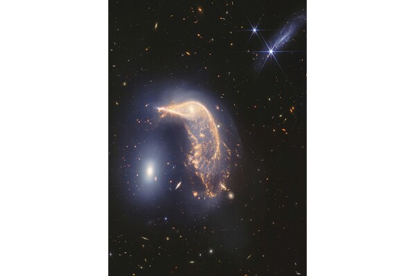 In this photo provided by NASA and the Space Telescope Science Institute, two interacting galaxies are captured by the Webb Space Telescope in the infrared. Scientists say the neighboring galaxies, nicknamed Penguin, right, and the Egg, left, have been tangled up for tens of millions of years. (NASA and Space Telescope Science Institute via AP)