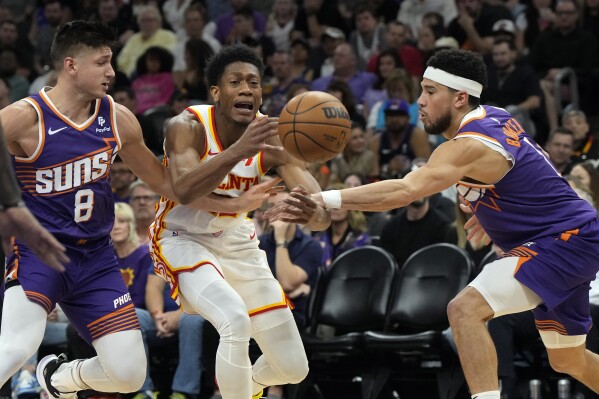 Atlanta Hawks forward De'Andre Hunter drives between Phoenix Suns guard Grayson Allen (8) and guard Devin Booker during the first half of an NBA basketball game, Thursday, March 21, 2024, in Phoenix. (AP Photo/Rick Scuteri)