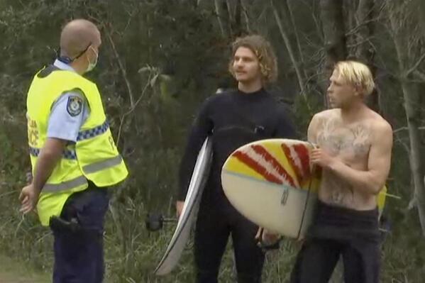 In this image made from a video, a policeman talks to surfers near a beach in Coffs Harbour, Australia Sunday, Sept. 5, 2021. A surfer was fatally bitten by a shark off Australia's eastern coast Sunday as many locals went to beaches to celebrate Father's Day. (Australian Broadcasting Corporation via AP)