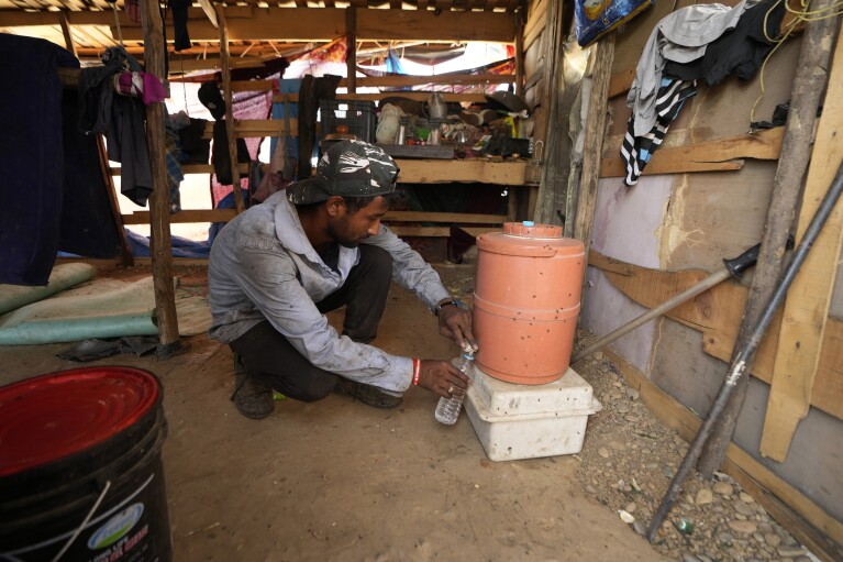 Aamir Shekh fills up his water bottle before working at a garbage dump during a heat wave on the outskirts of Jammu, India, Wednesday, June 19, 2024. Shekh and his family are among millions of people who scratch out a living searching through India's waste — and climate change is making a hazardous job more dangerous than ever. (AP Photo/Channi Anand)