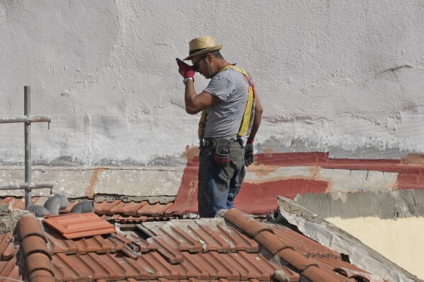 A worker pauses in the heat on a roof of a building in Madrid, Spain, Tuesday, Aug. 8, 2023. Spain is set to experience several days of extreme heat with temperatures in many parts set to rise above 40 degrees Celsius (104 degrees Fahrenheit). (AP Photo/Paul White)