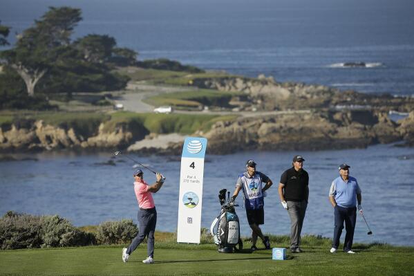 FILE - Rory McIlroy, of Northern Ireland, hits from the fourth tee of the Spyglass Hill Golf Course during the first round of the AT&T Pebble Beach National Pro-Am golf tournament Feb. 8, 2018, in Pebble Beach, Calif. Looking on from left are caddie Tim Mickelson, Phil Mickelson and Jimmy Dunne III. Dunne was instrumental in getting the PGA Tour to meet with the head of Saudi Arabia's wealth fund. (AP Photo/Eric Risberg, File)