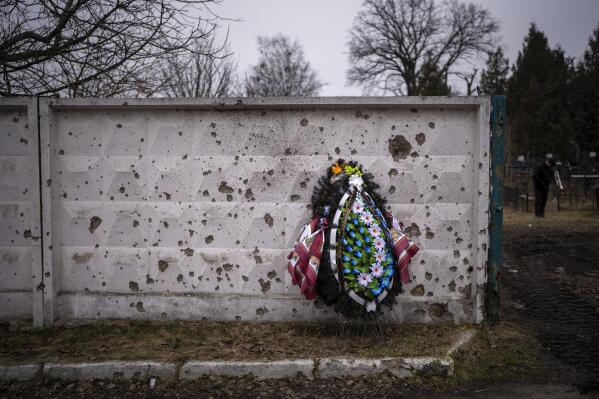 A wreath is photographed leaning against a shrapnel-damaged wall in the cemetery where the funeral for Kasich, 42, is being held, in Bucha, near Kyiv, Ukraine, Friday, Feb. 17, 2023. Kasich Kostiantyn, 42, as senior lieutenant of 93rd Ukrainian brigade was killed on Tuesday, Feb. 14 in the fightings in Bakhmut area. (AP Photo/Emilio Morenatti)
