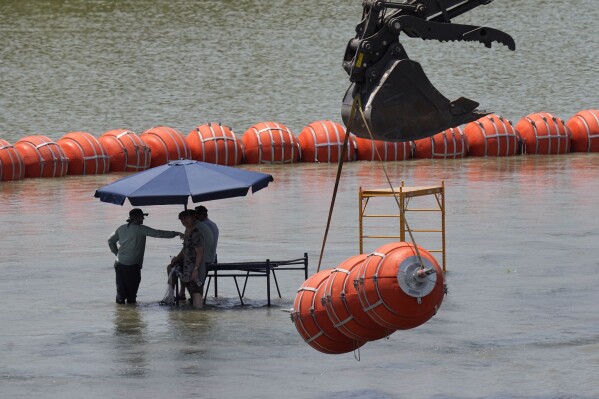 Workers take a break from deploying large buoys to be used as a border barrier along the banks of the Rio Grande in Eagle Pass, Texas, Wednesday, July 12, 2023. The floating barrier is being deployed in an effort to block migrants from entering Texas from Mexico. (AP Photo/Eric Gay)