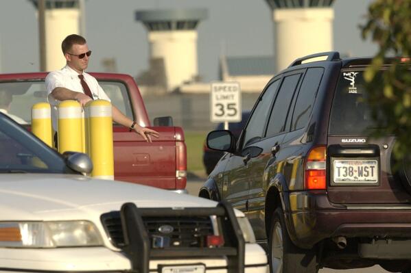 FILE - Vehicles are checked as they enter the Federal Bureau of Prisons complex, Wednesday, June 2, 2004 in Beaumont, Texas.Seven inmates have been charged with killing two fellow prisoners and wounding two others during a January, 2022 attack the a federal prison in Texas that led to a nationwide lockdown of the federal prison system a 15-count indictment filed this week said. (AP Photo/David J. Phillip)