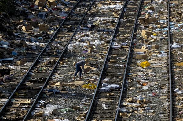 A member of the media picks up a shredded box at a section of the Union Pacific train tracks in downtown Los Angeles, Friday, Jan. 14, 2022. Thieves have been raiding cargo containers aboard trains nearing downtown Los Angeles for months, leaving the tracks blanketed with discarded packages. The sea of debris left behind included items that the thieves apparently didn't think were valuable enough to take, CBSLA reported Thursday. (AP Photo/Ringo H.W. Chiu)