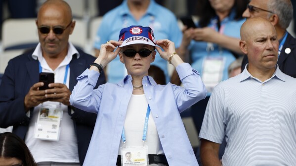 Ex-American soccer player Megan Rapinoe adjusts her cap as she waits for the start of the quarterfinal women's soccer match between the U.S. and Japan at Parc des Princes at the 2024 Olympics on Saturday, Aug. 3, 2024, in Paris, France. (AP Photo/Aurelien Morissard)