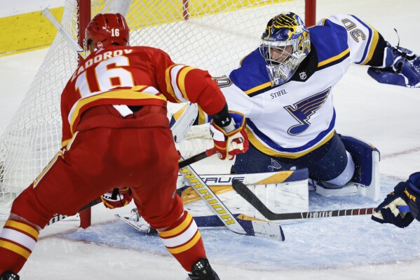 St. Louis Blues goalie Joel Hofer (30) blocks a shot by Calgary Flames defenseman Nikita Zadorov, left, during third-period NHL hockey game action in Calgary, Alberta, Thursday, Oct. 26, 2023. (Jeff McIntosh/The Canadian Press via AP)