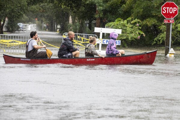 Trip Hamilton paddles his friends Brandin Gates, second from left, Mallie Taylor, second from right, and Ellie Combs, right, all from Charleston, S.C., in a canoe down Ashley Ave in Charleston as Tropical Storm Debby approaches, Tuesday, Aug. 6, 2024. (AP Photo/Mic Smith)