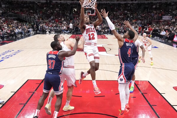 Chicago Bulls' Ayo Dosunmu (12) drives to the basket between Washington Wizards' Eugene Omoruyi (97) and Jared Butler (4) during the first half of an NBA basketball game Saturday, March 16, 2024, in Chicago. (AP Photo/Charles Rex Arbogast)