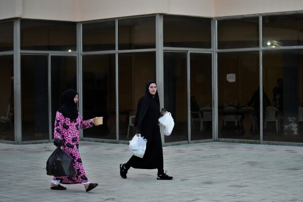 Residents displaced from her home in southern Lebanon by clashes on the border with Israel carry food on Friday, March 15, 2024. Roughly 60 displaced families are sheltering at an abandoned hotel in the town of Marwanieh, Lebanon, and are celebrating the Islamic holy month of Ramadan there. (AP Photo/Bilal Hussein)