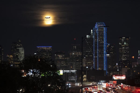 A Southwest Airlines plane makes its final approach at Dallas Love Field Airport near a the full moon and downtown Dallas buildings, Monday, Nov. 27, 2023. More Americans are expected to fly or drive far from home over Christmas than did last year, putting a cap on a busy year for travel. (AP Photo/Julio Cortez)