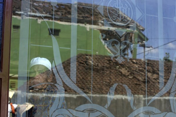 
              A man looks out from a mosque window as damaged homes are reflected on a glass window in the Kekait village affected by Sunday's earthquake in North Lombok, Indonesia, Wednesday, Aug. 8, 2018. (AP Photo/Firdia Lisnawati)
            