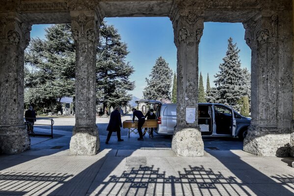 Undertakers carry a coffin out of a hearse at Bergamo's cemetery, northern Italy, Monday, March 16, 2020. Bergamo is one of the cities most hit by the new coronavirus outbreak in northern Italy. For most people, the new coronavirus causes only mild or moderate symptoms. For some it can cause more severe illness, especially in older adults and people with existing health problems. (Claudio Furlan/LaPresse via AP)