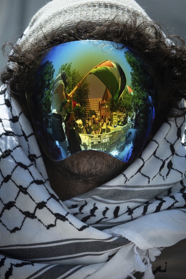 A Palestinian flag is reflected in a demonstrator's mask as students protest the Israel-Hamas war at George Washington University in Washington, Sunday, April 28, 2024. Protests and encampments have sprung up on college and university campuses across the country to protest the war. (AP Photo/Cliff Owen)