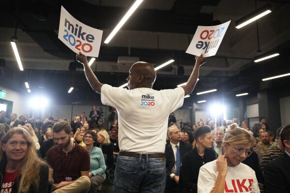 In this Feb. 5, 2020, photo, campaign worker Wendell McCoy hands out signs at a campaign event for Democratic presidential candidate and former New York City Mayor Michael Bloomberg, in Providence, R.I. (AP Photo/David Goldman)