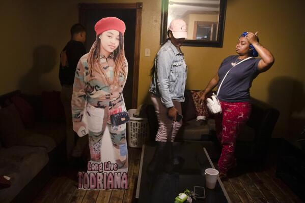 A cutout of Todriana Peters stands in her living room with her cousin Brione Rogers and mother Katrina Lambert in New Orleans, Thursday, July 8, 2021. Twelve-year-old Todriana Peters was shot and killed outside a graduation party on Memorial Day Weekend in the Lower 9th Ward neighborhood. Homicide rates in many American cities have continued to rise although not as precipitously as the double-digit jumps seen in 2020 and still below the violence of the mid-90s. (AP Photo/Sophia Germer)