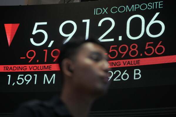 A man stands near an electronic board displaying stock prices at the Indonesia Stock Exchange, in Jakarta, Indonesia, Tuesday, April 8, 2025. (AP Photo/Achmad Ibrahim)