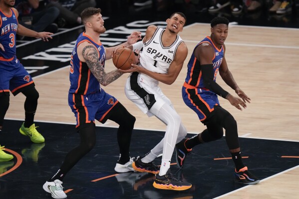 New York Knicks' Isaiah Hartenstein, left, and RJ Barrett, right, try to get the ball from San Antonio Spurs' Victor Wembanyama during the first half of an NBA basketball game, Wednesday, Nov. 8, 2023, in New York. (AP Photo/Seth Wenig)