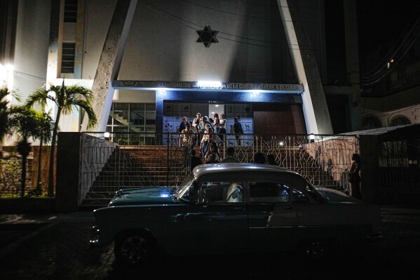 An American classic car sits parked in front of the Beth Shalom synagogue as Jews exit after attending a Shabbat service, in Havana, Cuba, Friday, Feb. 16, 2024. At Cuba's largest synagogue, ancient Jewish traditions and Cubanness often blend. (AP Photo/Ramon Espinosa)