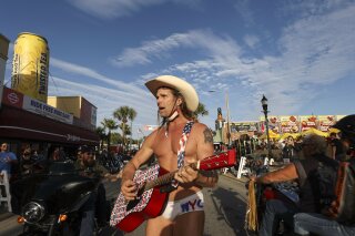 Robert Burck, better known as the Naked Cowboy, walks down the middle of Main Street while performing in Daytona, Fla., during the start of Bike Week on Friday, March 5, 2021. Police arrested the Times Square performer on a misdemeanor resisting arrest charge and cited him for panhandling as he worked a gig at Bike Week.  (Sam Thomas/Orlando Sentinel via AP)