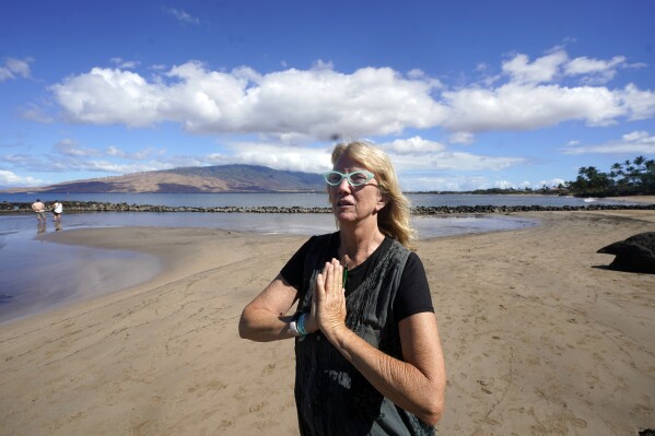 Anne Landon walks along a beach, Tuesday, Aug. 15, 2023, in Kihei, Hawaii. The evacuation center at the South Maui Community Park Gymnasium is now Landon’s safe space. She has a cot and access to food, water, showers, books and even puzzles that bring people together to pass the evening hours. (AP Photo/Rick Bowmer)