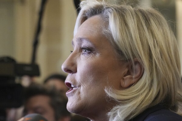 French far-right leader Marine Le Pen, center, answers reporters at the National Assembly and confirmed the National Rally party will vote against Prime Minister Michel Barnier in an upcoming no-confidence vote, Monday, Dec. 2, 2024 in Paris. (AP Photo/Michel Euler)