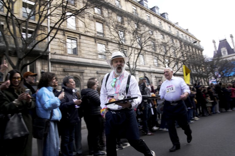 Οι σερβιτόροι κουβαλούν δίσκους με ένα φλιτζάνι καφέ, ένα κρουασάν και ένα ποτήρι νερό καθώς συμμετέχουν σε μια διαδρομή σερβιτόρου στους δρόμους του Παρισιού, Κυριακή 24 Μαρτίου 2024. (AP Photo/Christophe Ena)