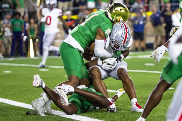 Notre Dame safety Ramon Henderson, left, and cornerback Cam Hart, bottom, stop Ohio State receiver Emeka Egbuka at the goal line late in the fourth quarter of an NCAA college football game Saturday, Sept. 23, 2023, in South Bend, Ind. (AP Photo/Michael Caterina)