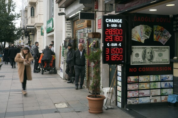 Peple walk next to an exchange currency shop in Istanbul, Turkey, Thursday, Dec. 21, 2023. Turkey's central bank hiked its key interest rate by 2.5 percentage points on Thursday as part of its efforts to combat high inflation that has left many households struggling to afford rent and essential items. (AP Photo/Khalil Hamra)