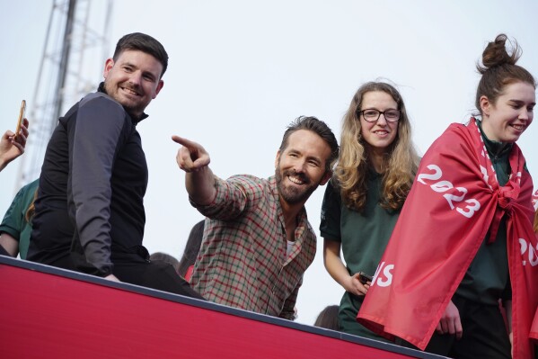 FILE - Wrexham co-owner Ryan Reynolds, center, celebrates with members of the Wrexham FC soccer team the promotion to the Football League in Wrexham, Wales, on May 2, 2023. Wrexham was down on its luck and languishing in the fifth tier of English soccer before being given the A-list treatment by Reynolds and co-owner Rob McElhenney. Now it is embarking on a U.S. tour this month and fans of the globally-streamed docuseries “Welcome to Wrexham” will get to see its unlikely stars in the flesh. (AP Photo/Jon Super, File)