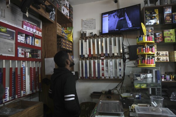 A man watches a replay of security camera footage on Sunday, Jan. 7, 2024, in a smoke shop in the occupied West Bank village of Beit Rima. The footage, taken two days earlier from outside the shop, shows three Palestinians being shot in the village square by Israeli forces, one of them fatally.  (AP Photo/Mahmoud Illean)