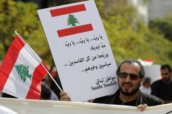 
              A Lebanese protester holds an Arabic placard that reads: "Hey God, extend your hands and comfort us from all the corrupt, the politicians and the others," during a protest against corruption and criticizing long-serving politicians for failing to form a government, in Beirut, Lebanon, Thursday, Nov. 22, 2018. Lebanon is marking 75 years of independence with a military parade Thursday in Beirut, but many anxious Lebanese feel they have little to celebratemeq. (AP Photo/Hussein Malla)
            