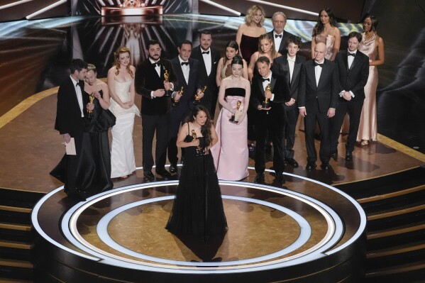 Samantha Quan, front center, accepts the award for best picture for "Anora" during the Oscars on Sunday, March 2, 2025, at the Dolby Theatre in Los Angeles. Alex Coco, from rear left, Darya Ekamasova, Lindsey Normington, Vache Tovmasyan, Karren Karagulian, Vincent Radwinsky, Luna Sofía Miranda, Mikey Madison, Sean Baker, Mark Eydelshteyn, Yura Borisov, Meg Ryan, and Billy Crystal look on from back. (AP Photo/Chris Pizzello)