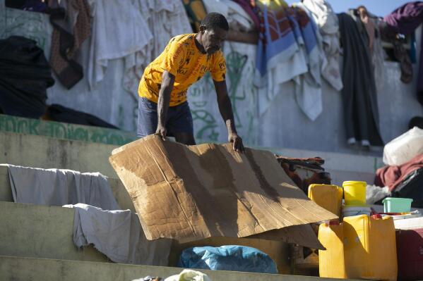 A man dries a piece of cardboard he uses to sleep on at the Hugo Chavez public square transformed into a refuge for families forced to leave their homes due to clashes between armed gangs in Port-au-Prince, Haiti, Thursday, Oct. 20, 2022. (AP Photo/Odelyn Joseph)