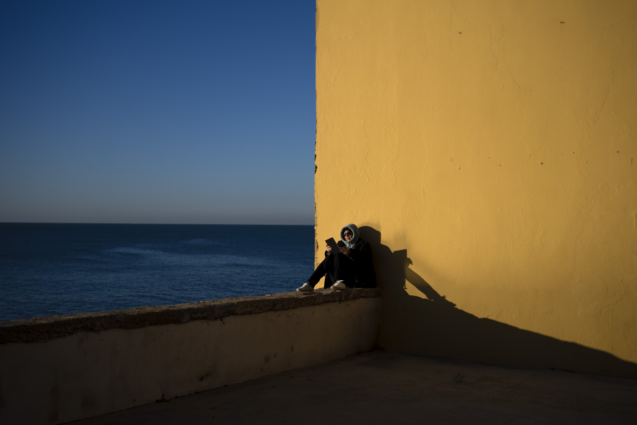 A woman reads by the sea while the first rays of sunlight fall on the city of Cadiz, Spain, on Jan. 27, 2023. (AP Photo/Emilio Morenatti)