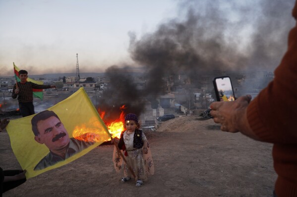 A child holds a flag showing Kurdish leader Abdullah Ocalan as he has his picture taken during Nowruz celebrations, in Amuda, Hasaka region, northeastern Syria, Thursday, March 20, 2025. (AP Photo/Baderkhan Ahmad)