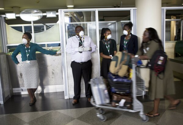 Travellers and airport staff, some wearing masks as a precaution against the coronavirus outbreak, walk through Robert Mugabe International airport in Harare, Wednesday, March, 11, 2020. For most people, the new coronavirus causes only mild or moderate symptoms, such as fever and cough. For some, especially older adults and people with existing health problems, it can cause more severe illness, including pneumonia. (AP Photo/Tsvangirayi Mukwazhi)