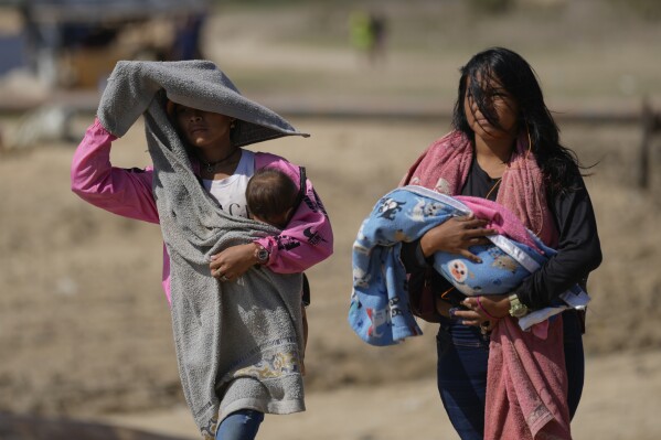 Women carry babies after arriving by boat from La Bulla Loca mine, which collapsed, in La Paragua, Bolivar state, Venezuela, Friday, Feb. 23, 2024. The collapse of the illegally operated open-pit gold mine in a remote area of central Venezuela killed at least 16 people. (AP Photo/Ariana Cubillos)