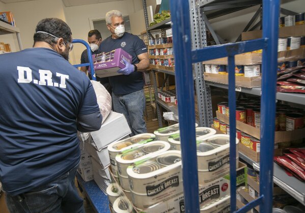 Veterans Response members, from left, Pablo Soto, Ray Guasp,  and Dan Torres, stock shelves at New Opportunities on West Main Street in Meriden, Conn., on Thursday,  April 23, 2020. The non-profit organization is collecting and distributing mostly non-perishable food items to local pantries throughout the state. (Dave Zajac /Record-Journal via AP)