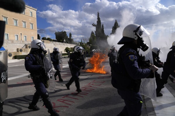 Riots police stand in front of the Parliament as a fire from a molotov cocktail is seen in the background during a students demonstration in Athens, Greece, Friday, March 8, 2024. Thousands of protesters have gathered in central Athens to oppose government plans to introduce privately-run universities, following weeks of demonstrations including scores of university building occupations by students. Lawmakers were to vote on the measure later Friday with the bill expected to pass. (AP Photo/Thanassis Stavrakis)