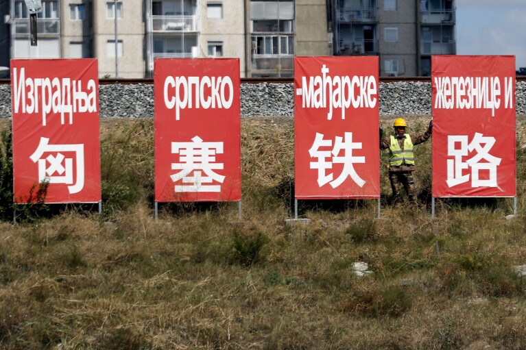 FILE - A worker rests between billboards that read: ''Construction of the Serbian-Hungarian railway'' in Belgrade, Serbia, Friday, Sept. 4, 2020. In 2014, Hungary and Serbia concluded an agreement with Beijing to modernize the railway between their capitals of Budapest and Belgrade, part of a Belt and Road plan to link up with the Chinese-controlled port of Piraeus in Greece, to the south, an entry point for Chinese goods to Central and Eastern Europe. (AP Photo/Darko Vojinovic, File)