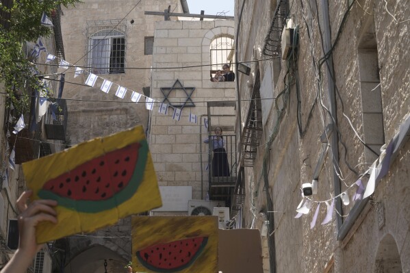 FILE - Jewish girls watch Israelis and Palestinians holding pictures of watermelon, a Palestinian symbol, as they protest the imminent eviction of a Palestinian family by a Jewish settler organization outside their home in the Muslim Quarter of the Old City of Jerusalem, June 16, 2023. (AP Photo/Mahmoud Illean, File)