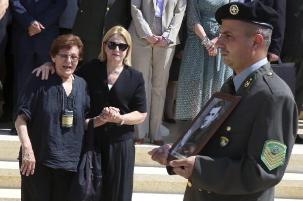 Family members watch as a soldier holding a photograph of a Greek soldier whose remains were recently identified leads an honor guard at a funeral service at Ayios Panteleimonas Orthodox Church in the Cypriot capital Nicosia, Thursday, May 30, 2024. The service was held for 15 recently identified Greek soldiers who died in Cyprus fighting against invading Turkish troops nearly half a century ago.(AP Photo/ Philippos Christou)