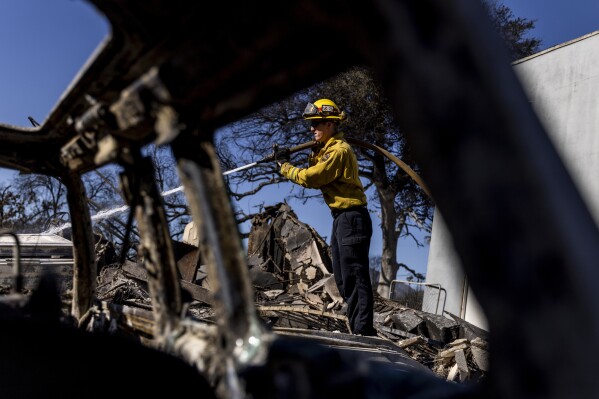 Mike Hassler, a firefighter with Cal Fire Nevada-Yuba-Placer Unit, hoses down a hotspot at a home destroyed by the Eaton Fire in Altadena, Calif., Sunday, Jan. 12, 2025. (Stephen Lam/San Francisco Chronicle via AP)